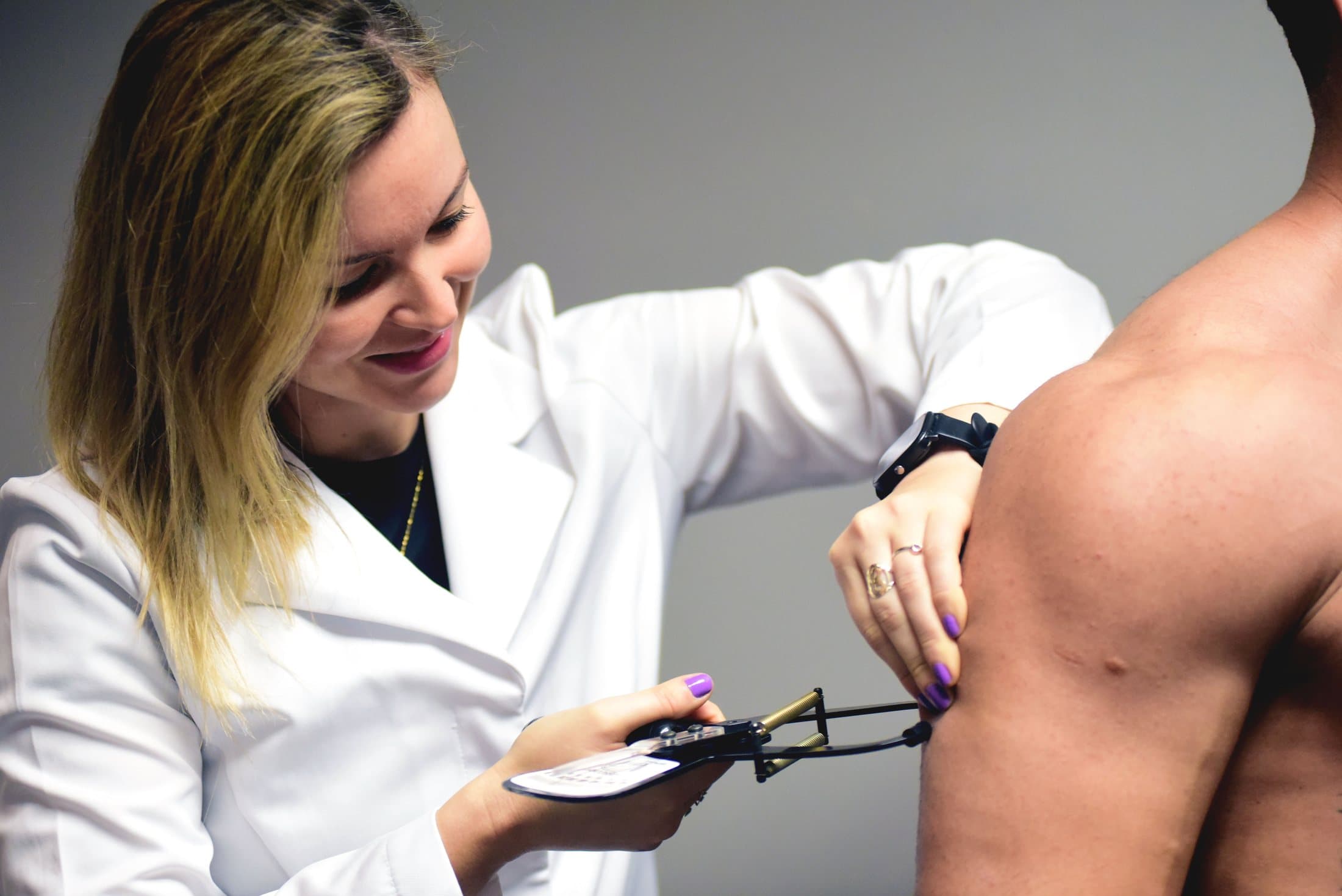 Carine fazendo avaliação física com adipômetro no braço de um aluno