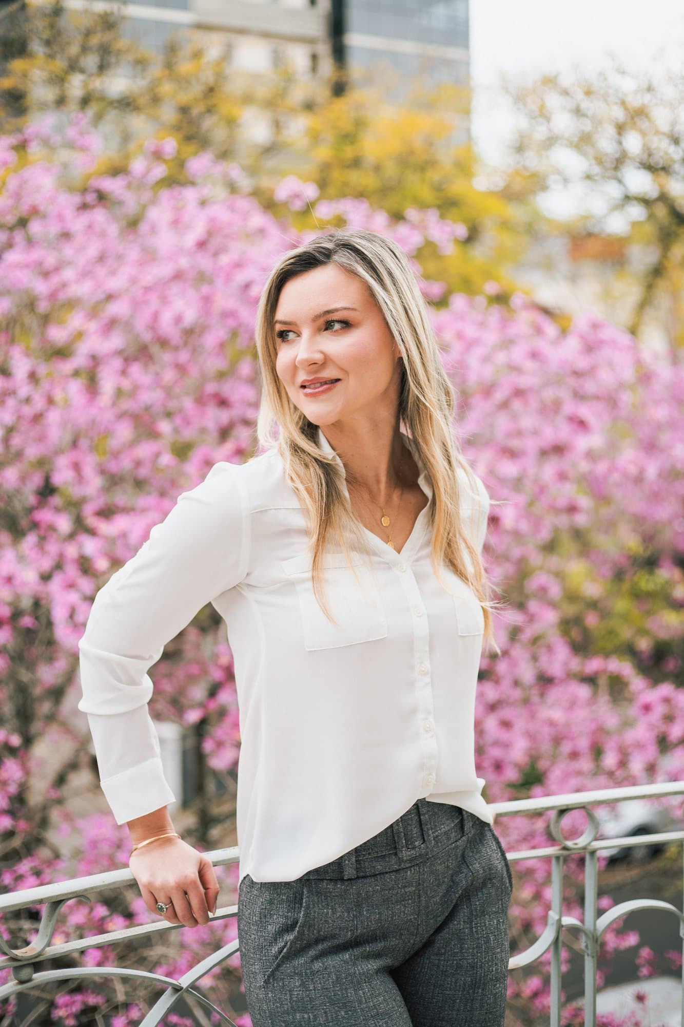 Carine Salatti de camisa branca, apoiada num gradil, diante de uma árvore florida